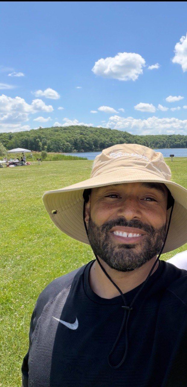 Frank Smith III smiling outdoors with a lake and open sky behind him