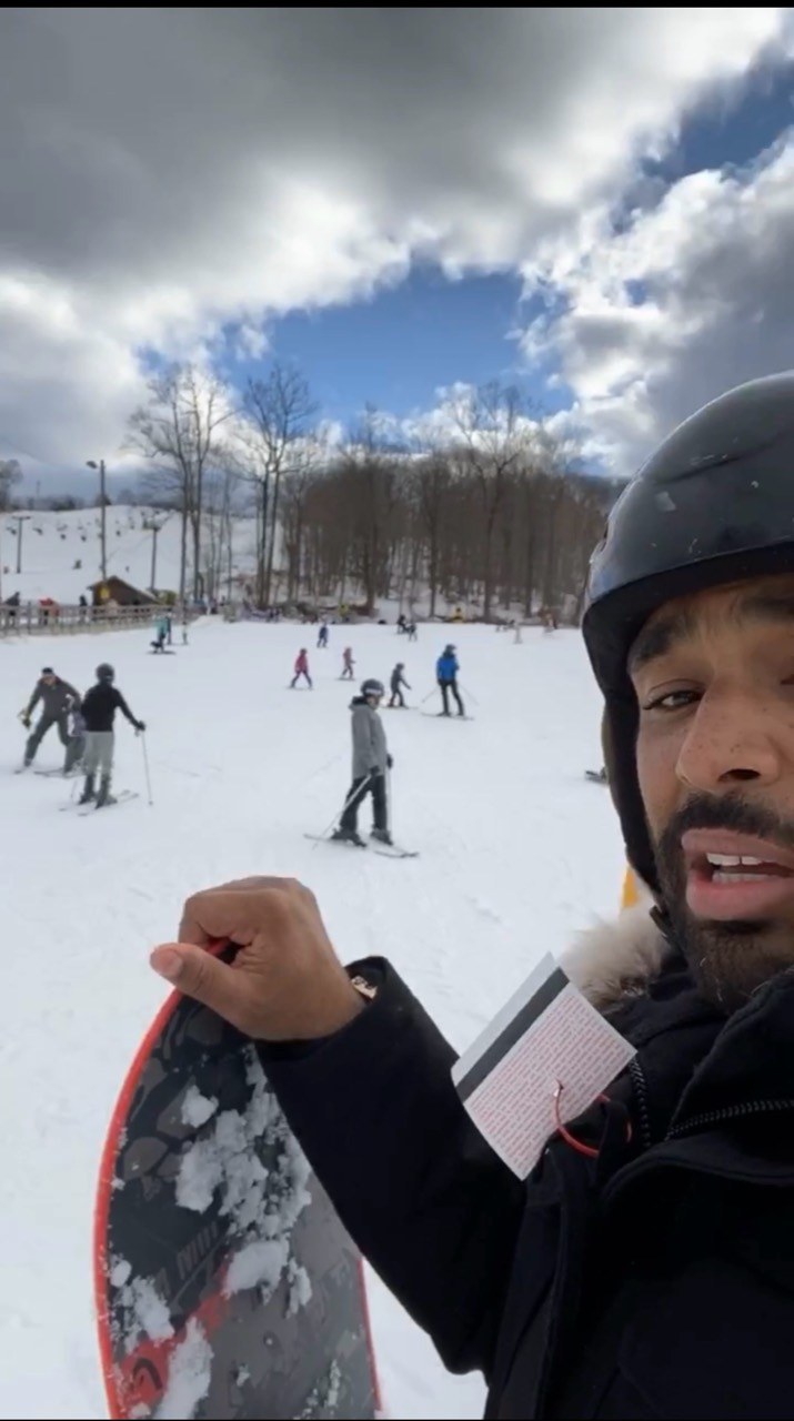 Frank Smith III holding a snowboard beside a snowy slope