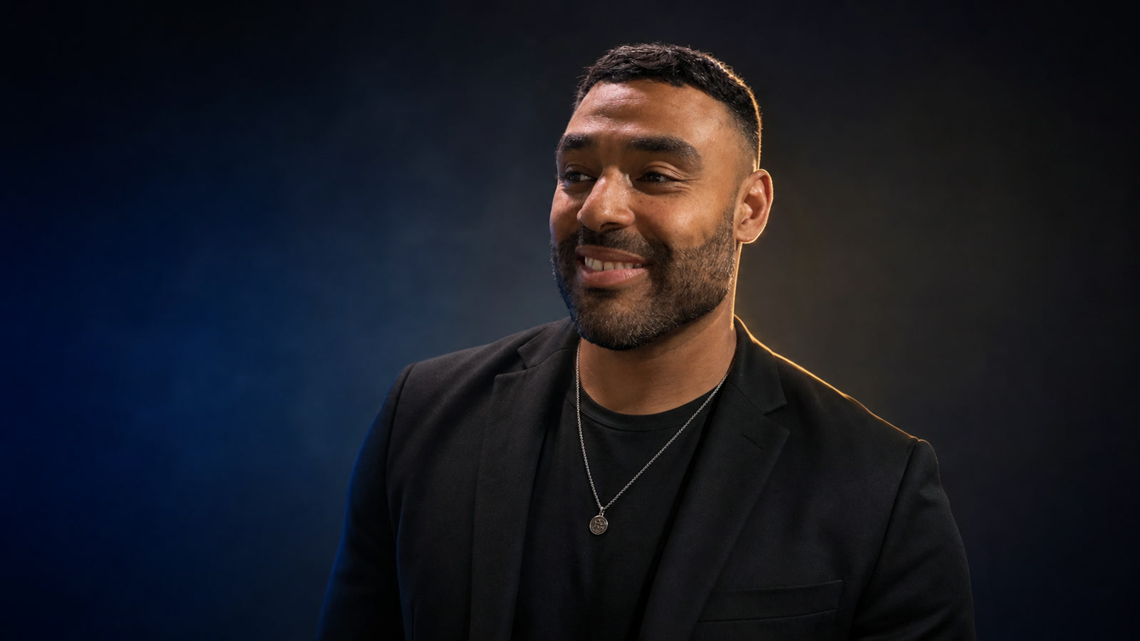 Frank Smith III in a matte black blazer against a dark blue cinematic studio background